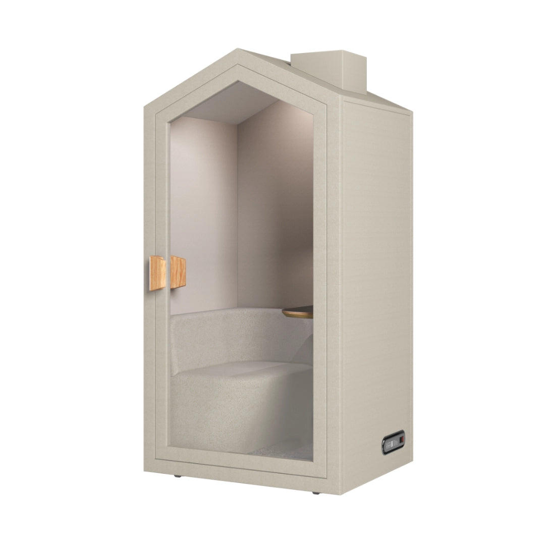 The product is an acoustic meeting pod designed for private conversations or focused work. It features a cottage-like design with a light, neutral color scheme and a glass door. Inside, there is a comfortable seating area and a small wooden shelf, creating a cozy and functional space for meetings or calls.