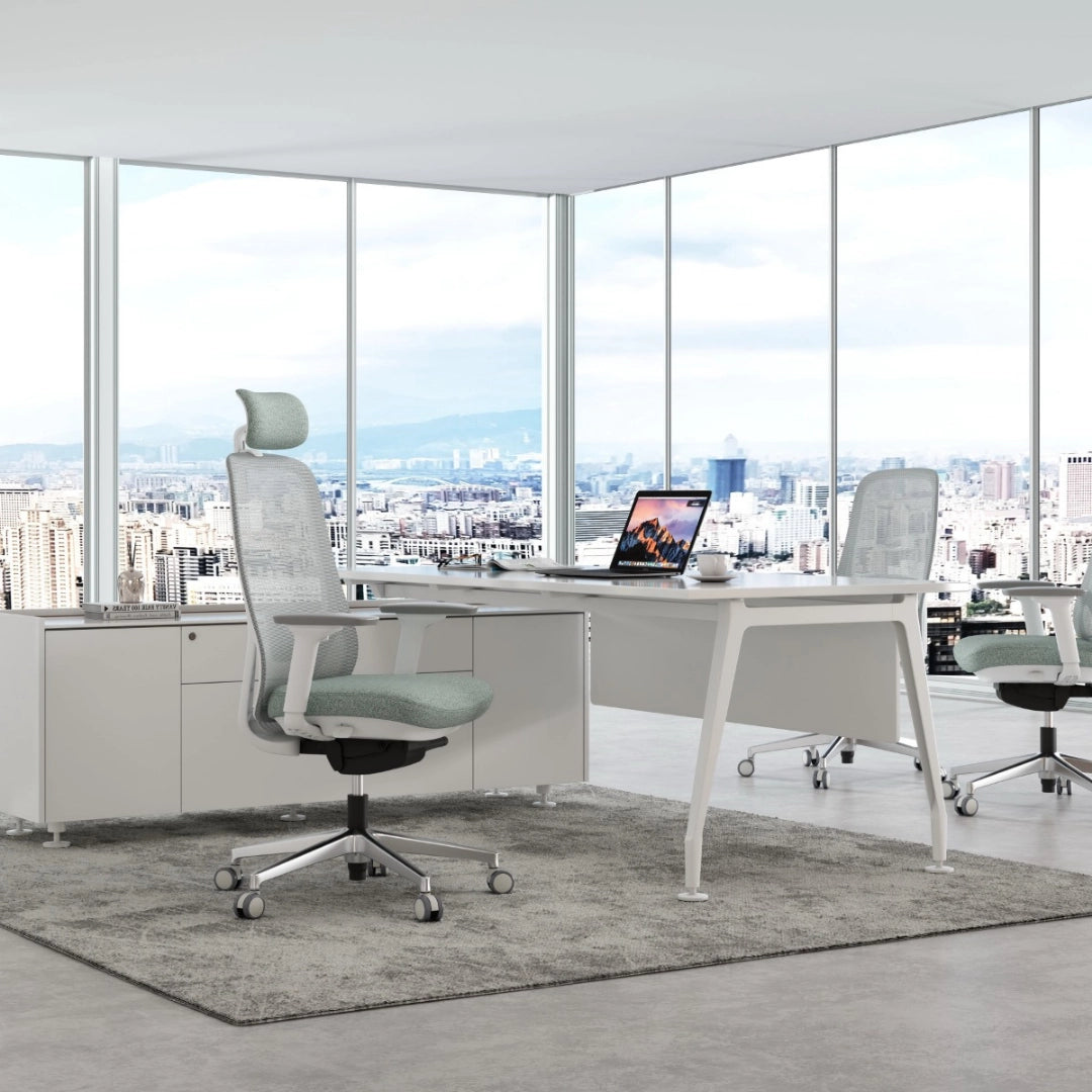 The image features an ergonomic office chair, likely from the brand Glory, designed for comfort and support during long hours of work. The chair has a mesh back and a soft seat cushion, positioned in a modern office environment with large windows showcasing a city view. A sleek desk with a laptop and a coffee cup is also visible, enhancing the contemporary workspace aesthetic
