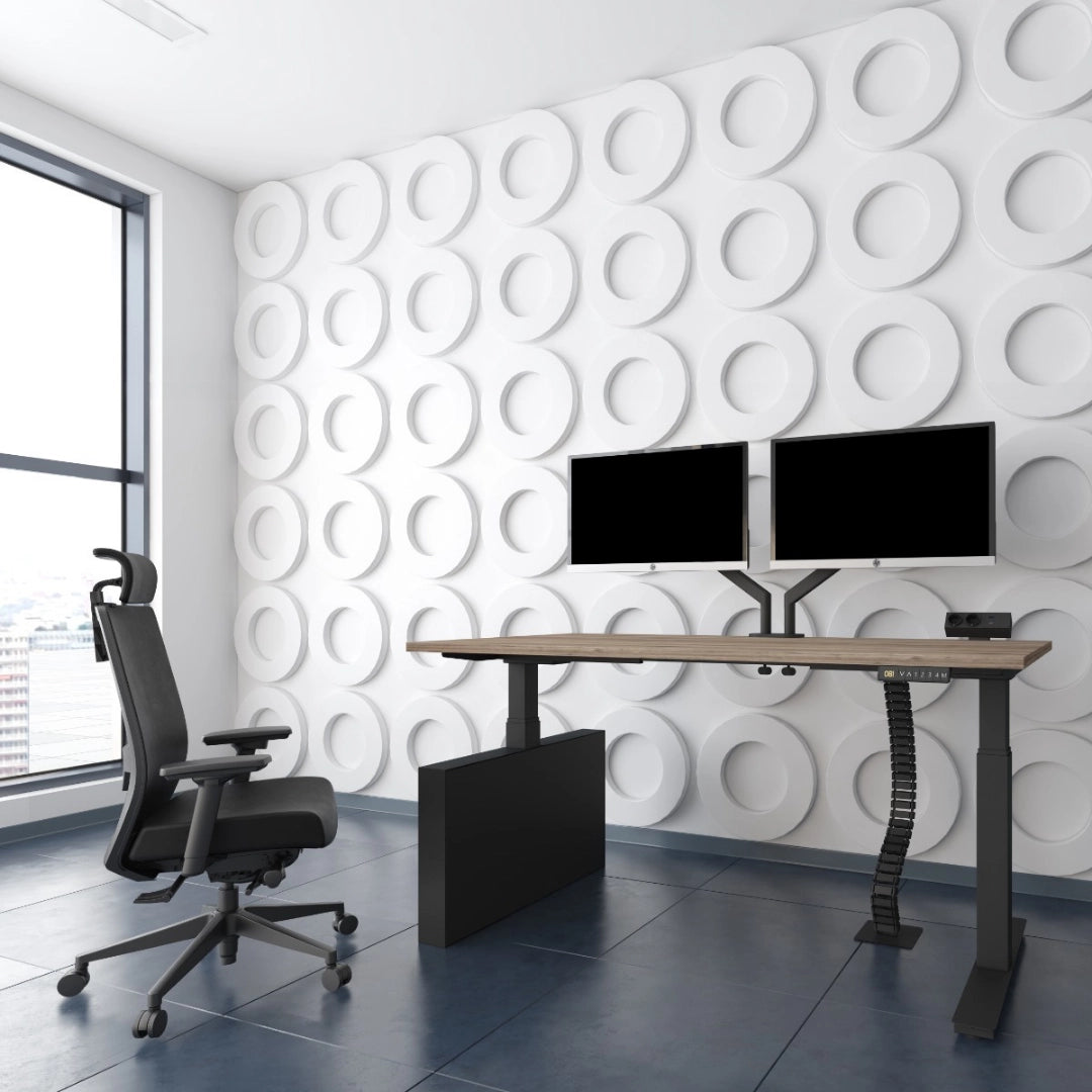 The image features an ergonomic office chair, designed for comfort and support during long hours of work. The chair is positioned next to a modern standing desk equipped with dual monitors. The room has a sleek, contemporary aesthetic with a textured white wall and large windows allowing natural light to enter.