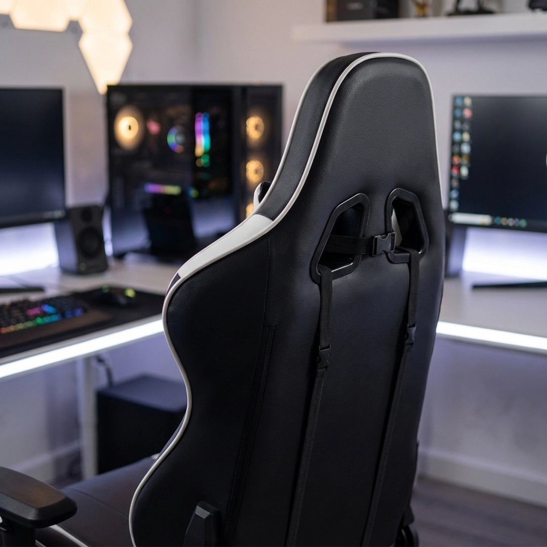 The image features a gaming chair, specifically the UVI Sport XL model in white and black. The chair has an ergonomic design with a high backrest and is positioned in a modern gaming setup, showcasing multiple monitors and RGB lighting in the background.
