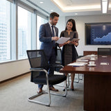The image features a conference chair with a sledge base design, suitable for office environments. It appears to be a modern ergonomic chair, designed for comfort during meetings. In the scene, a man and a woman are discussing documents in a well-lit conference room, with a large table and a presentation screen displaying a graph in the background.