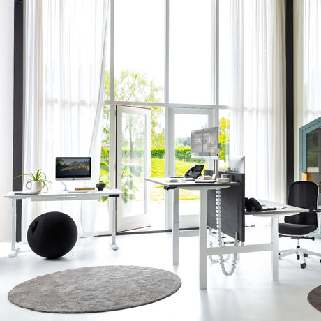 The image features an ergonomic seating ball, designed to promote better posture and active sitting. The setting includes a modern office space with large windows, a desk with a computer, and a stylish chair, creating a bright and inviting atmosphere. The seating ball is positioned on the floor, complementing the contemporary decor.