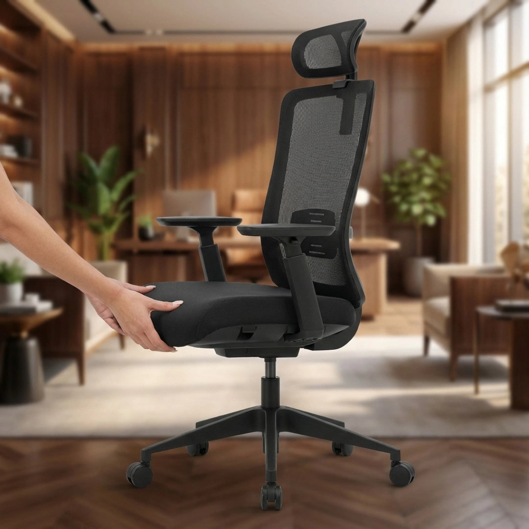 The product is an ergonomic office chair, specifically the Vane model. The image shows a person adjusting the chair, which features a sleek design with a mesh backrest and adjustable armrests. The setting appears to be a modern office or home workspace, with wooden furniture and plants in the background, emphasizing a comfortable and stylish environment.