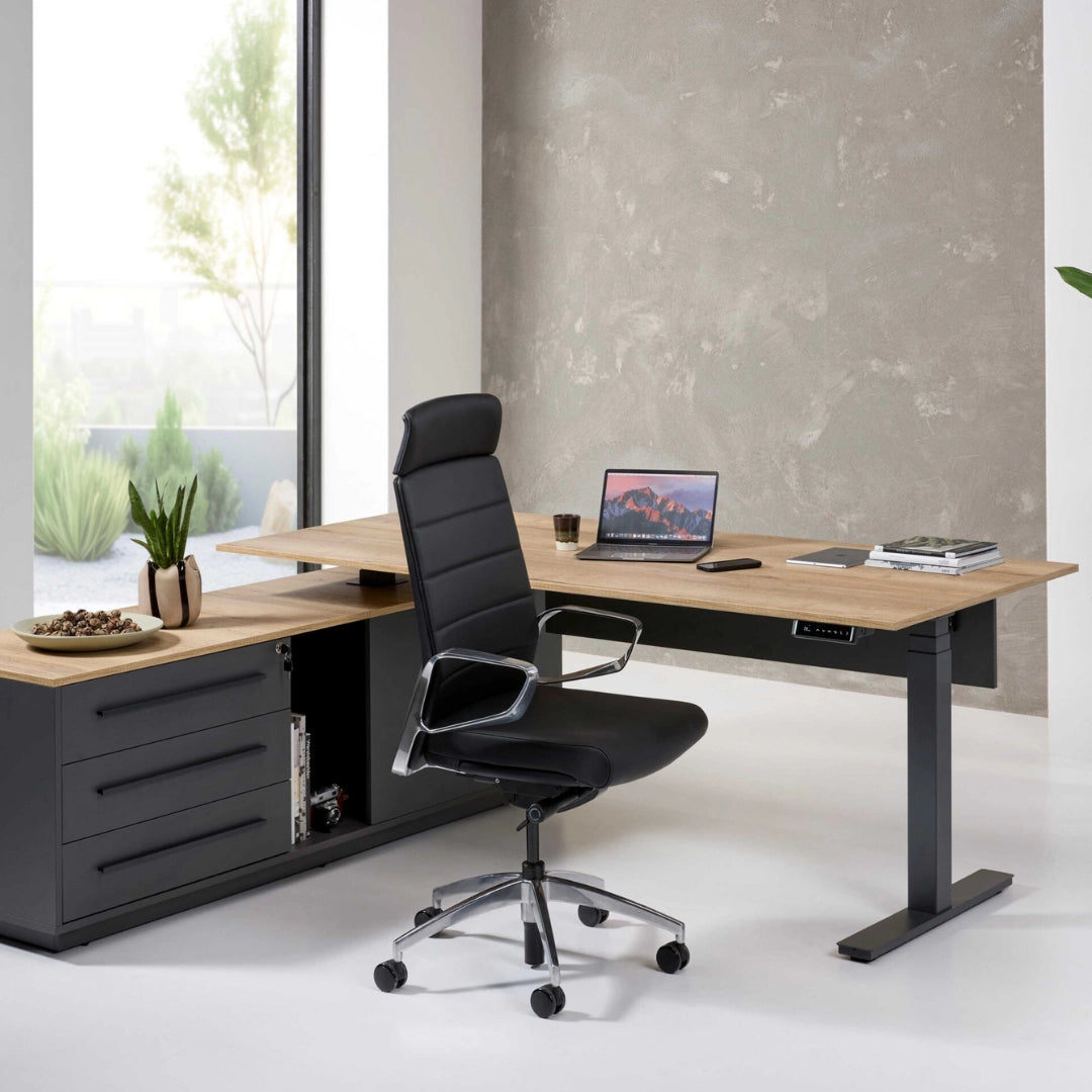 The image features an ergonomic office chair designed for executive use. It has a sleek black design with a high backrest and chrome accents. The chair is positioned in a modern office setting, which includes a stylish wooden desk, a laptop, and decorative elements like a plant and a bowl of nuts. The overall aesthetic is contemporary and professional.