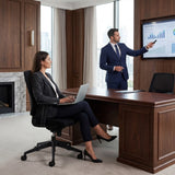 The image features an ergonomic office chair, designed for comfort and support during long hours of work. The setting is a modern office, where a woman is seated at a desk using a laptop, while a man in a suit presents information on a screen. The overall atmosphere conveys professionalism and collaboration.