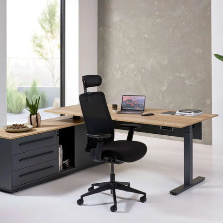 The image features an ergonomic office chair designed for comfort and support during long working hours. The chair is black with adjustable features, including a headrest and armrests. It is positioned next to a modern desk made of wood and metal, with a laptop, a glass, and some decorative items on the surface, creating a stylish and functional workspace.
