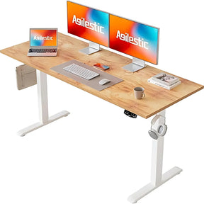 The product is a standing desk from the brand Agilestic. The desk features a wooden surface with a natural finish and a white frame. On the desk, there are two monitors displaying the Agilestic logo, a laptop, a keyboard, a mouse, a coffee cup, and a few books, creating a modern and organized workspace.