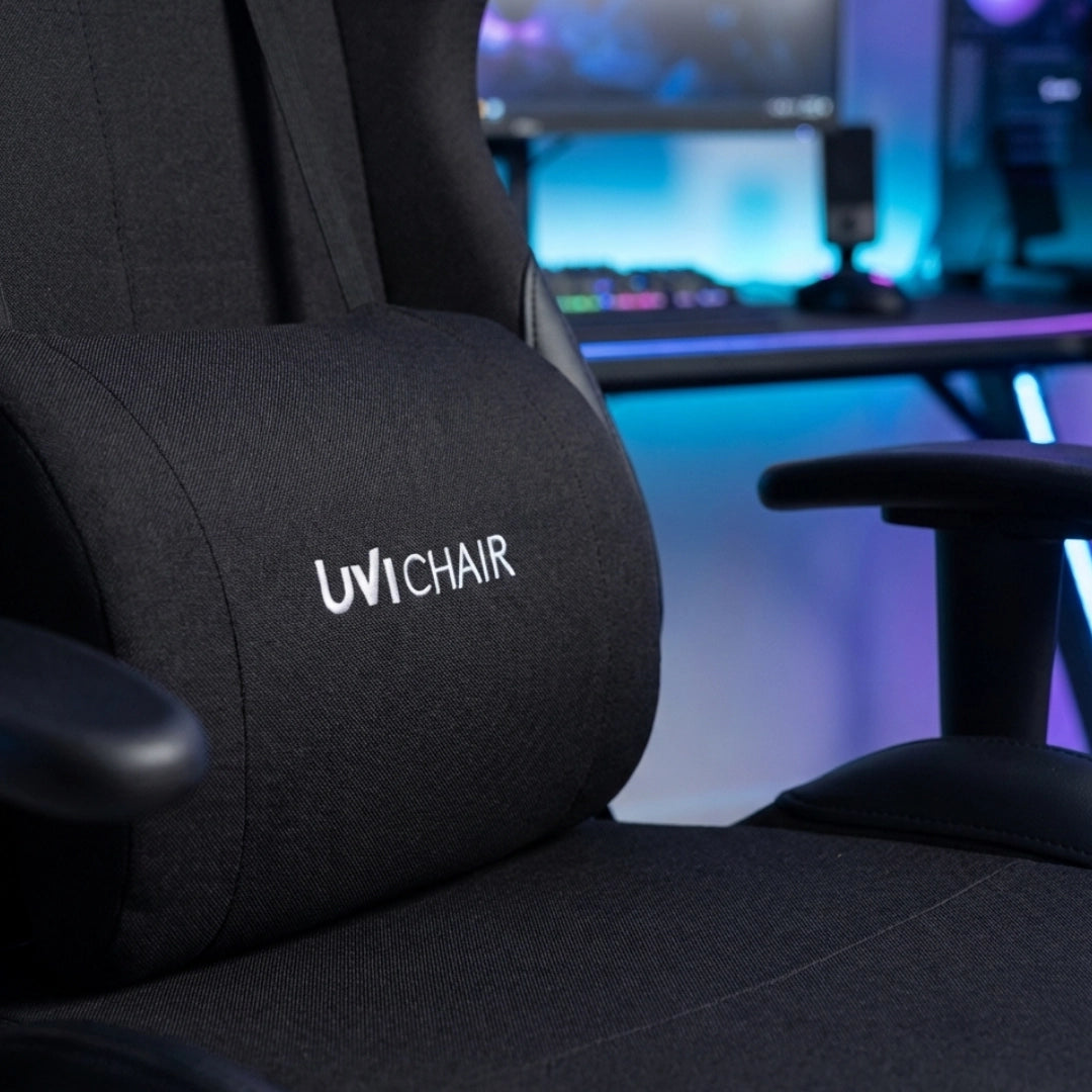The product is an ergonomic office chair designed for gaming, specifically the UVI Chair model. The image showcases a close-up of the chair's backrest and seat, featuring a sleek black fabric with the UVI Chair logo prominently displayed. The setting suggests a modern gaming environment with a colorful backdrop.