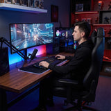The image features an ergonomic office chair designed for comfort during long hours of work or gaming. The chair is sleek and modern, likely from the brand UVI, model "Elegant Business." In the scene, a person is seated at a desk with a large curved monitor, gaming keyboard, and microphone, set against a backdrop of colorful ambient lighting and a