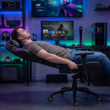 The image features an ergonomic office chair designed for comfort and support. It appears to be a model from the UVI brand, showcasing a user reclining in the chair. The setting includes a modern workspace with vibrant lighting and gaming equipment in the background, emphasizing a stylish and functional environment.