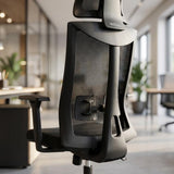 The product is an ergonomic office chair, specifically the UVI Focus model. The image shows the back of the chair, highlighting its sleek design with a mesh backrest for breathability. The chair features adjustable armrests and a modern aesthetic, set in a well-lit office environment with greenery in the background.