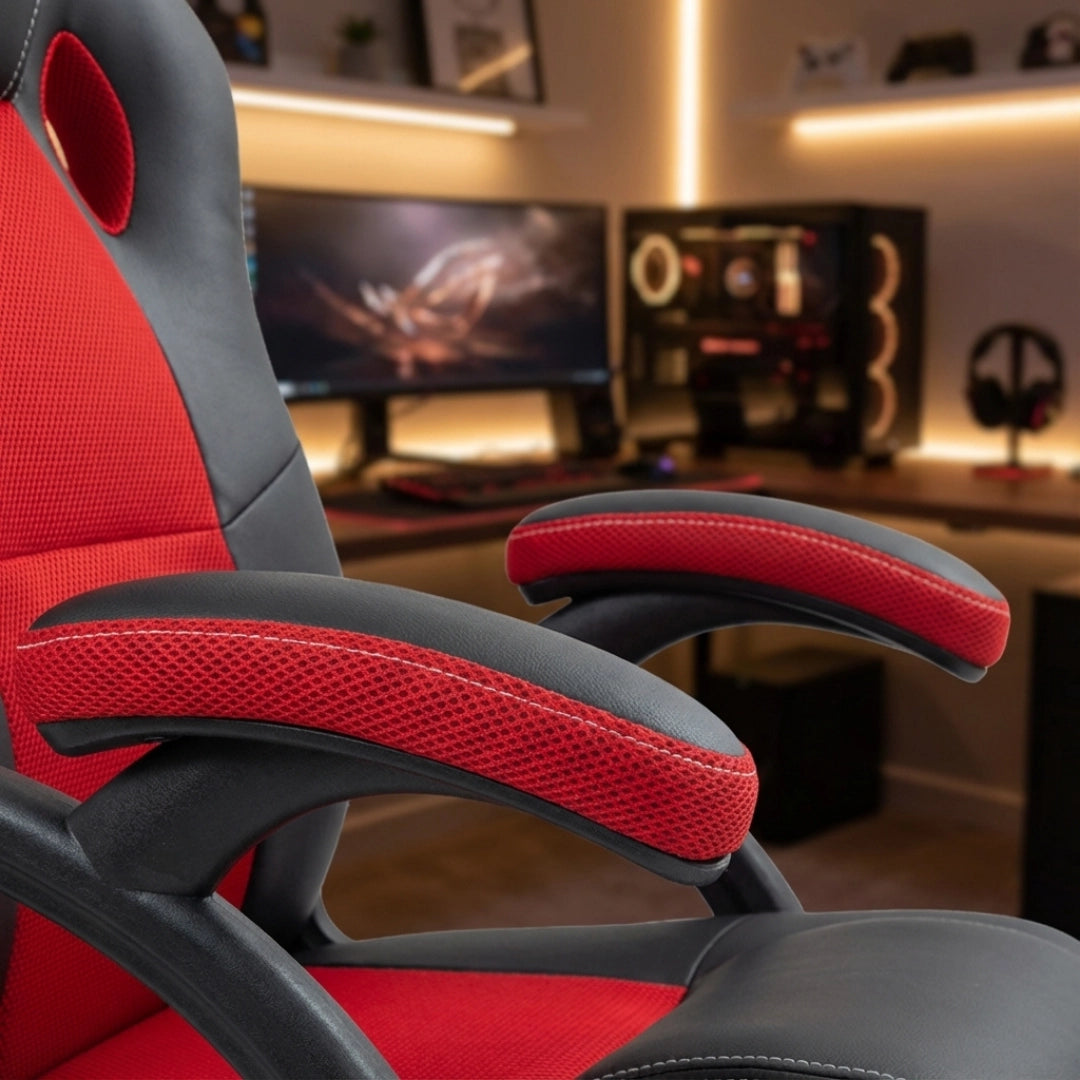The product is an ergonomic office chair, specifically the UVI Hero Red model. The image shows a close-up view of the chair's armrest, which features a combination of breathable mesh and padded material in red and black colors. The background includes a gaming setup with monitors and equipment, emphasizing its suitability for gaming and office use.