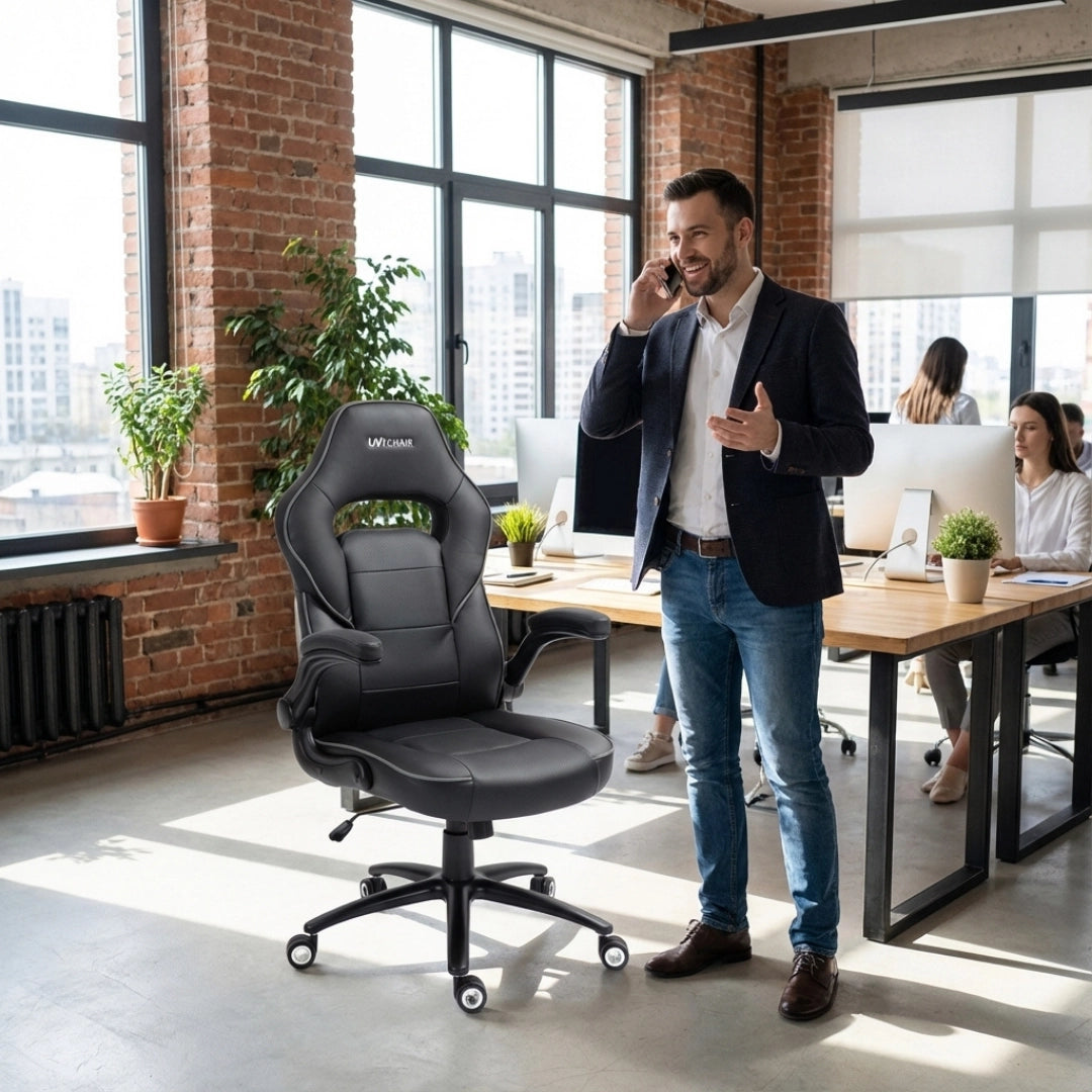 The product is an ergonomic office chair, specifically the UVI Simple Office model. The image shows a modern office environment with a man standing beside the chair while talking on the phone. The chair features a sleek black design with supportive cushioning, and there are several workstations visible in the background, indicating a collaborative workspace.