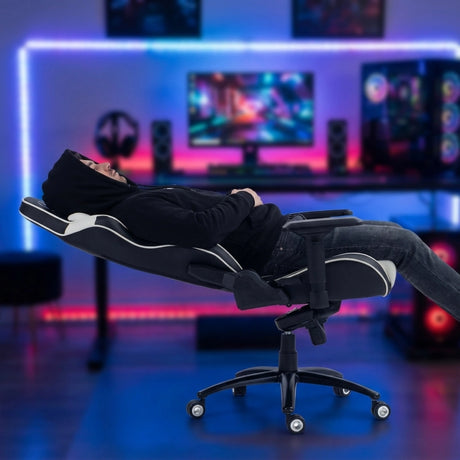 The image features an ergonomic gaming chair, specifically the UVI Sport XL model in white. It shows a person reclining in the chair, which is designed for comfort during extended gaming sessions. The background includes a colorful gaming setup with monitors and speakers, enhancing the gaming atmosphere.
