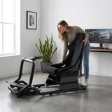 The image features a racing simulator seat, specifically the UVI Racing Seat Pro V2. It showcases a woman adjusting the seat, which has a sleek black design and ergonomic features suitable for gaming. The background includes a plant and a computer setup, indicating a modern gaming environment.