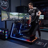 The image features a racing simulator setup, specifically the UVI Racing Simulator Extreme. It showcases a realistic racing seat, a steering wheel, and multiple monitors displaying a racing game environment. The setup includes ambient lighting and a modern design, emphasizing an immersive gaming experience. A person is seen adjusting the seat, highlighting the ergonomic aspect of the simulator.